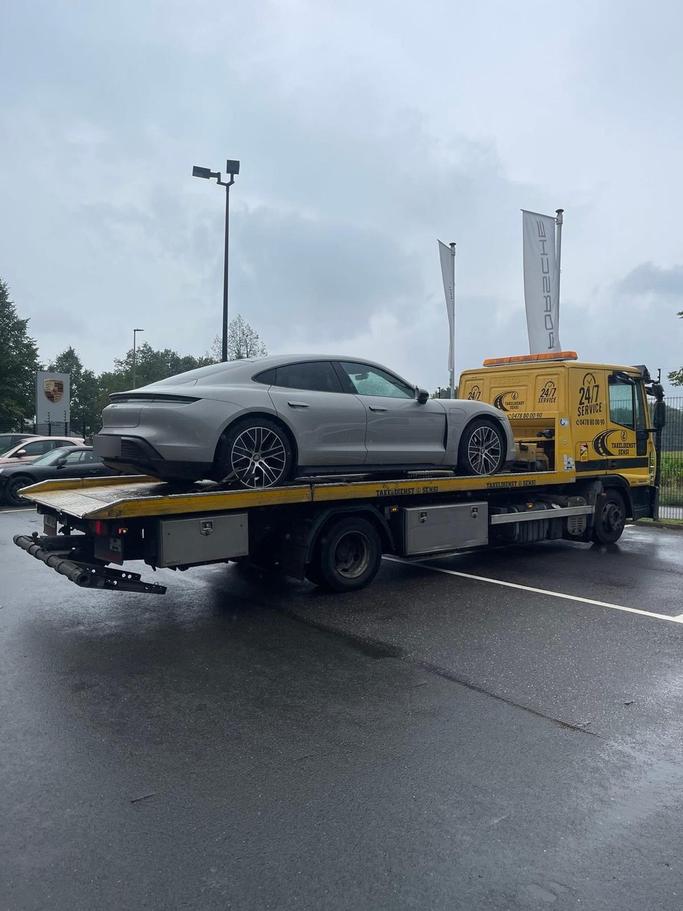 Grijze Porsche Taycan op de takelwagen bij een Porsche-dealer in de regen